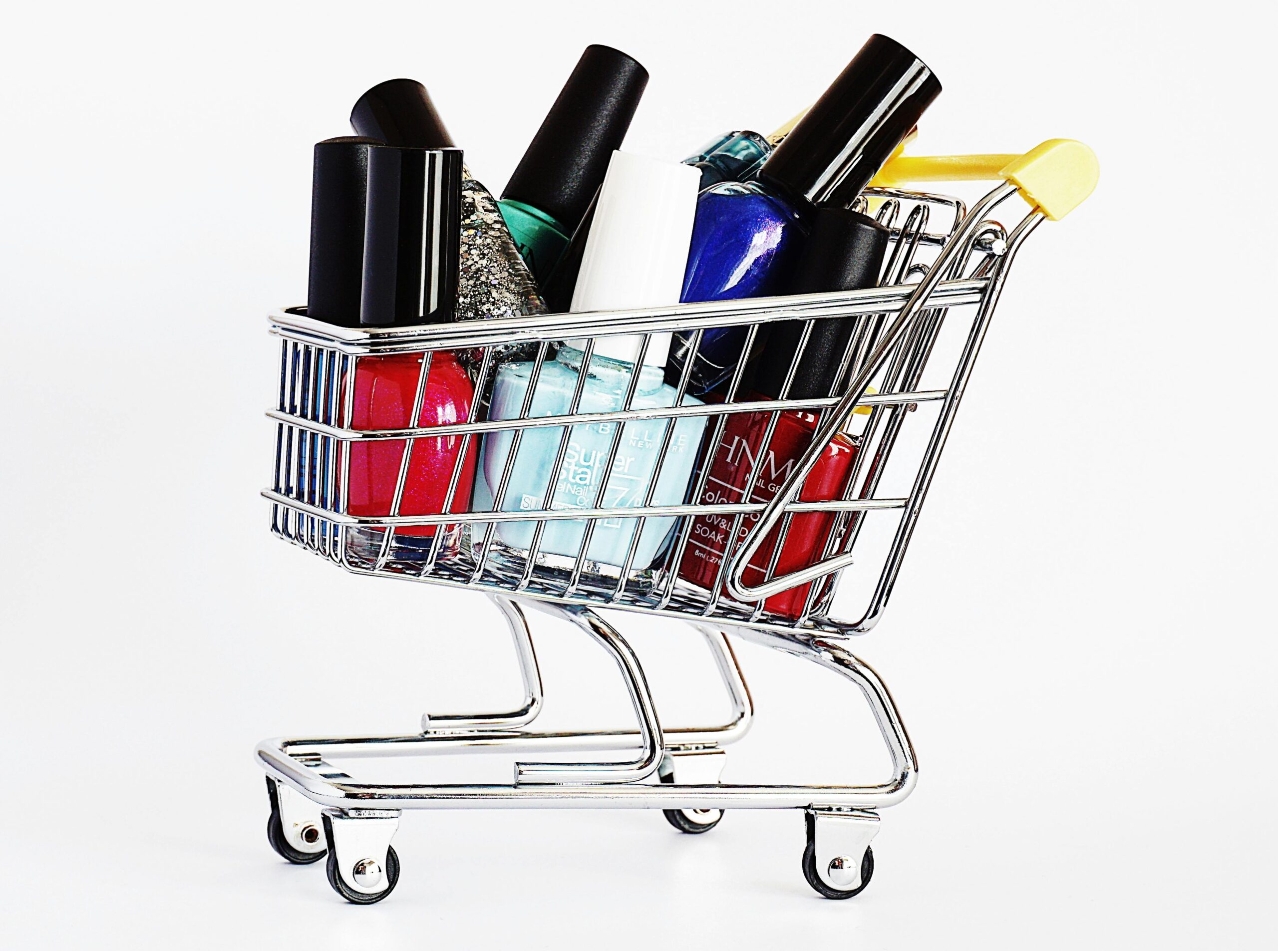 Colorful nail polish bottles in a mini shopping cart against white background.